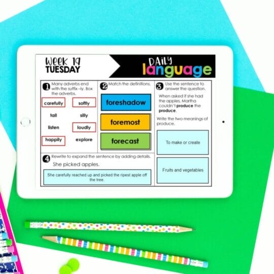 A tablet displays a weekly language activity worksheet on a blue and green background with two striped pencils, an eraser, and a colorful notebook nearby—perfect for 5th Grade Language Standards spiral review of adverbs, vocabulary, and sentence practice.